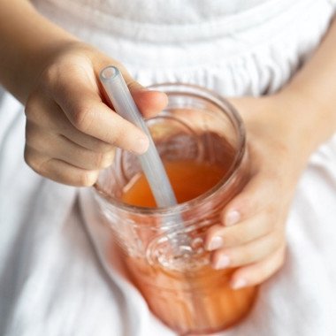 Fommi daugkartiniai silikoniniai šiaudeliai stiklinėje mergaitei ant kelių