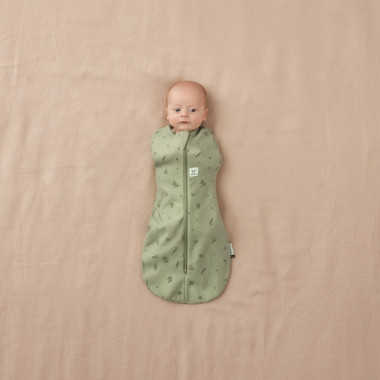 Lovytėje gulintis kūdikis su ergoPouch Swaddle žaliu miegmaišiu kūdikiui 0.2TOG (3-6 mėn.)