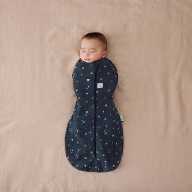 Kūdikis guli lovytėje su ergoPouch Swaddle tamsiai mėlynu miegmaišiu kūdikiui 1.0TOG (3-6 mėn.)