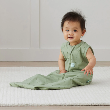 Kūdikis sėdi ant grindų ir dėvi ergoPouch Swaddle žalią miegmaišį 0.2TOG (8-24 mėn.)