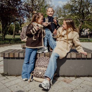 Trys mergaitės sėdi ant suoliuko, viena iš jų dėvi Pick & Pack vaikišką ergonominę mokyklinę kuprinę pradinukams Wild, M