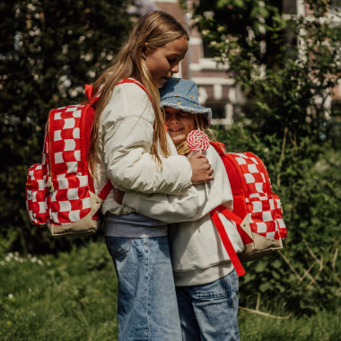 Dvi mergaitės apsikabinusios, viena iš jų dėvi Pick & Pack kuprinę pradinukams Raudoni langeliai, M