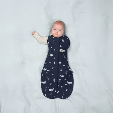 ergoPouch Swaddle miegmaišis kūdikiui 1.0TOG (3-6 mėn.) - tamsiai mėlyną dėvintis kūdikis su viena iškišta rankyte