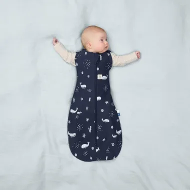 ergoPouch Swaddle miegmaišis kūdikiui 1.0TOG (3-6 mėn.) - tamsiai mėlyną dėvintis kūdikis su dviem iškištom rankytėm