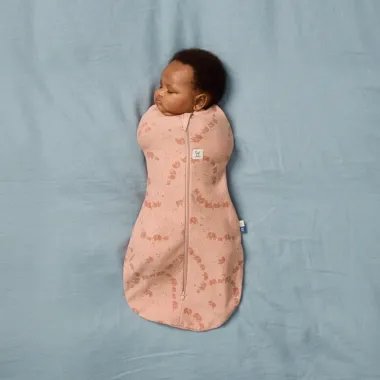 ergoPouch Swaddle miegmaišis kūdikiui 1.0TOG (0-3 mėn.) - kūdikis, gulintis ant mėlynos paklodės su kokoniuku