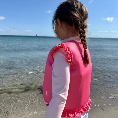 Mergaitė paplūdimyje dėvi rausvą plaukimo liemenę