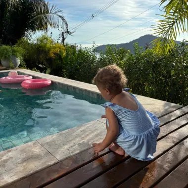 Mergaitė žaidžia su suknelės tipo maudymosi kostiumėliu prie baseino