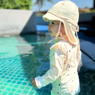 Mergaitė stovi prie baseino su šviesia maudymosi kepure